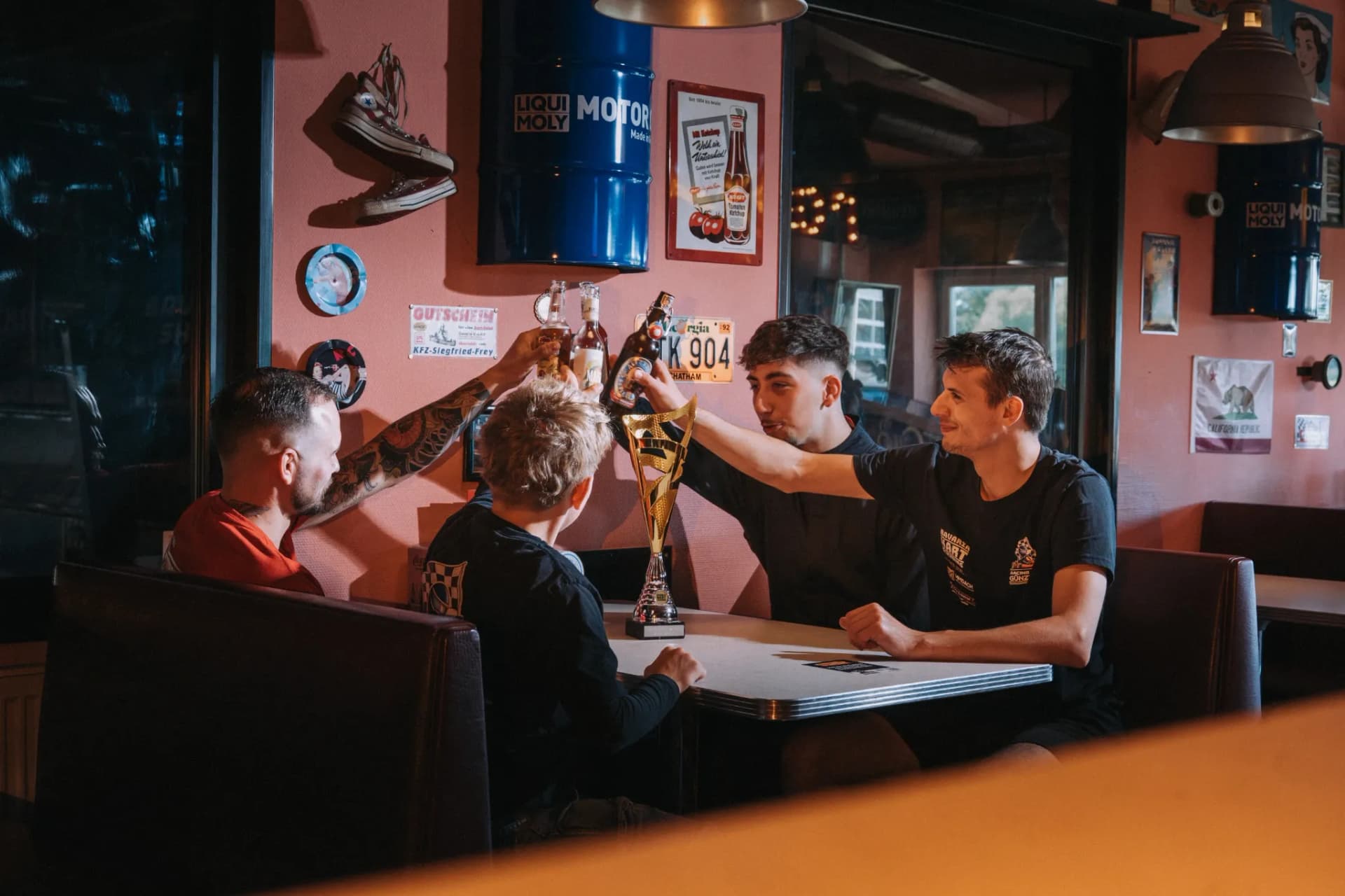 Fahrer stoßen im Bistro von Bavaria Kart mit dem Pokal auf dem Tisch an